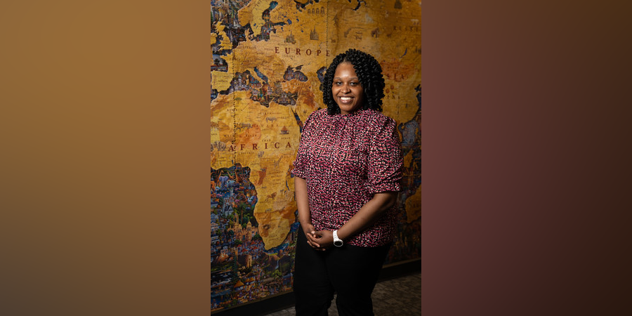 Abaneh Ebangwese stands in front of a gold map of Africa and Europe.