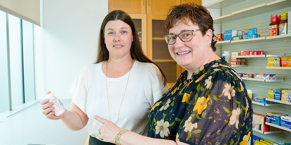 Amy Howard holding a white bottle of medication while Jill Morgan points at the bottle.
