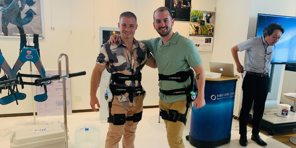 Two students wearing robotic equipment stand in a lab in Japan.