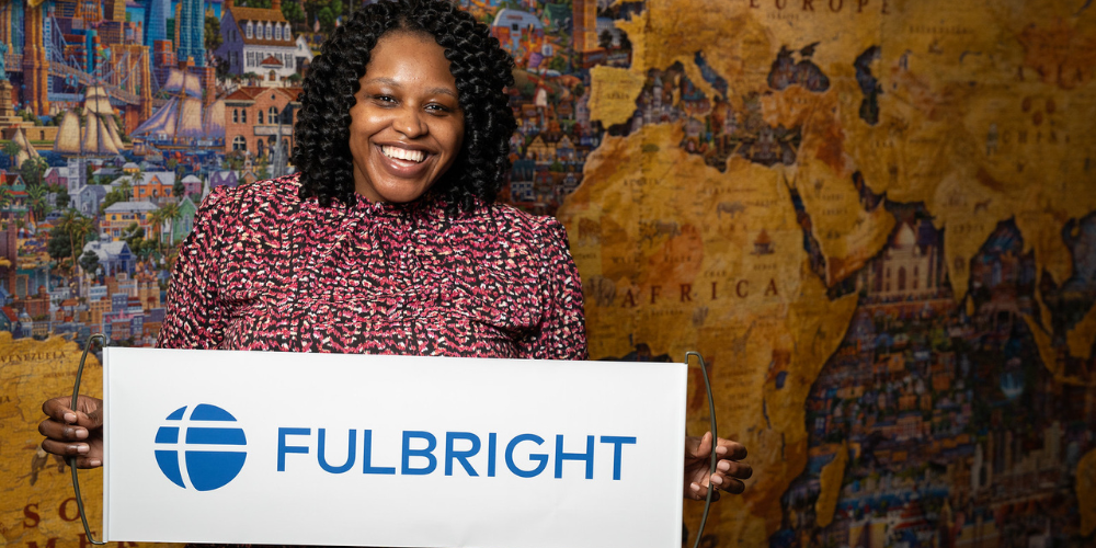 Abaneh Ebangwese holds a banner that says Fulbright in front of a giant map