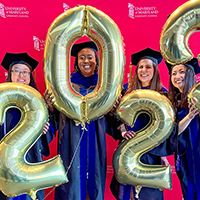 Four graduates holding 2023 balloons