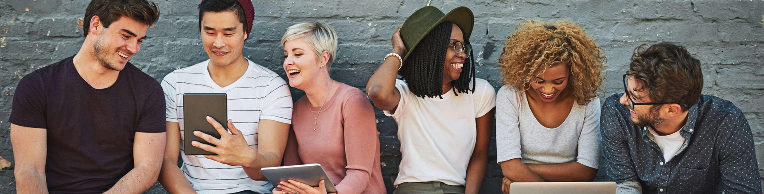 a diverse group of people sitting on a bench look at social media and enjoy one another's company