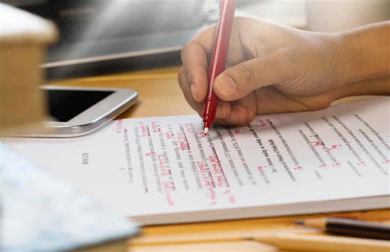 person editing a paper using a red pen