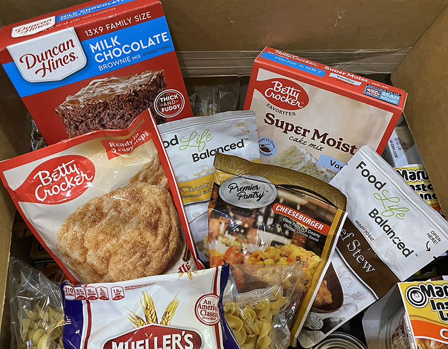 A donation box full of food, including baking supplies, pasta, and dry soup