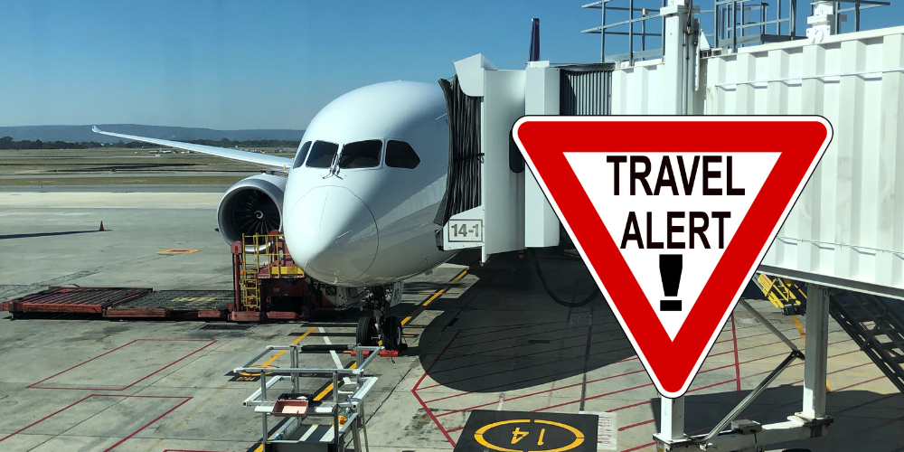 An airplane at the gate with a Travel Alert sign