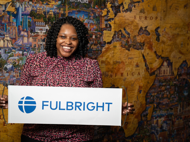 Abaneh Ebangwese holds a Fulbright banner in front of a large map