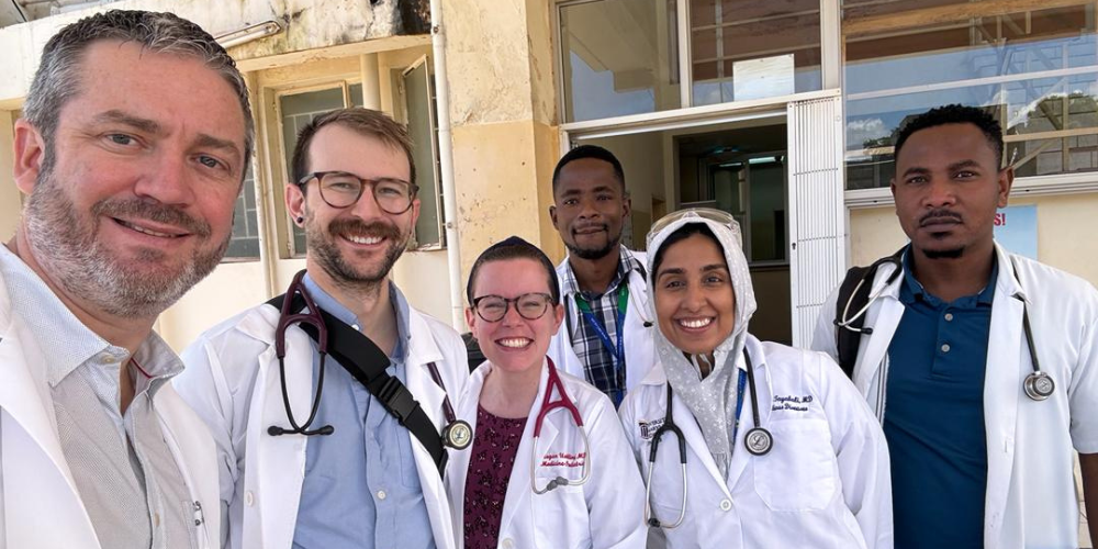 A group of students and faculty in medical jackets pose for a group photo in Zambia