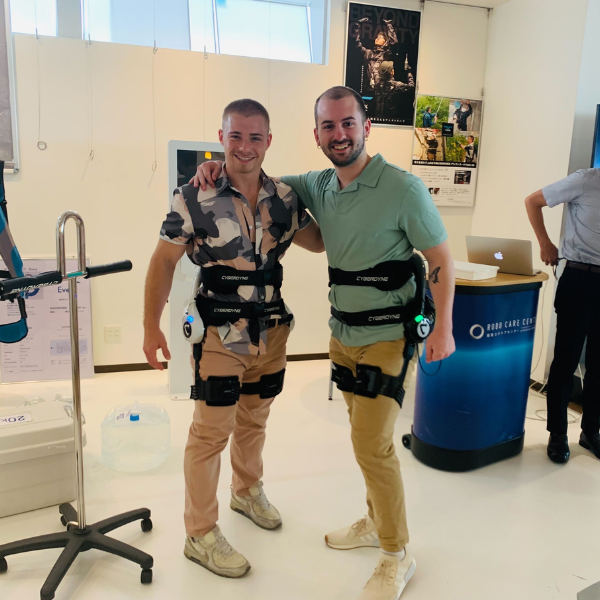 Two students pose together wearing robotic gear in a lab in Japan