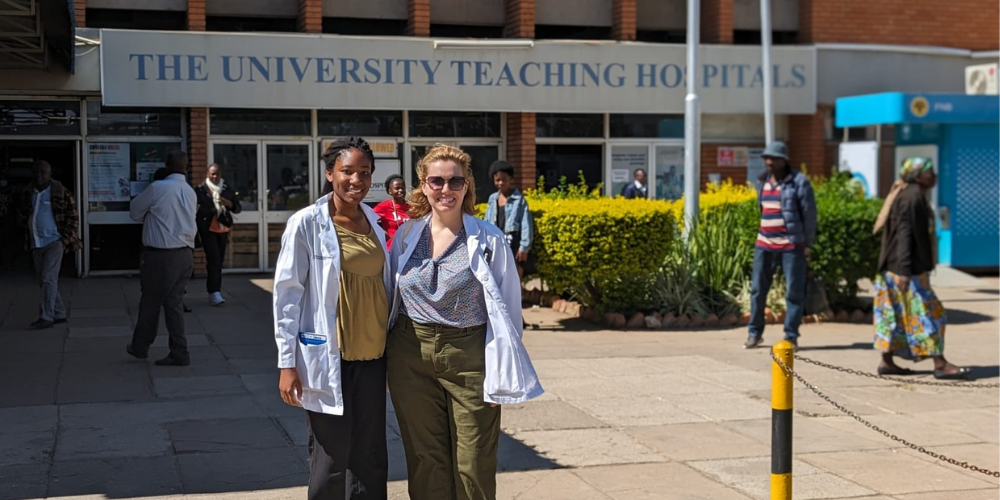 Two women in white coats stand outside the University Teaching Hospital in Zambia