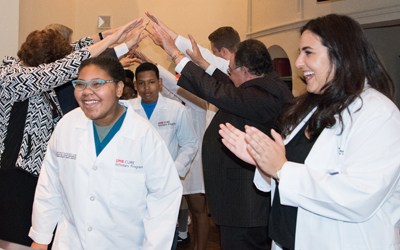 CURE Scholars emerge from a bridge of mentors' arms as UM School of Dentistry student Kathryn Pawlak, founder of Planet Smilez, looks on during a ceremony at the end of Planet Smilez Discovering Dentistry Camp.