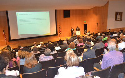 A large crowd at the University of Maryland, Baltimore forum on race listen to remarks by UMB President Jay A. Perman, MD, left, and Roger J. Ward, EdD, JD, MPA, chief accountability officer and vice president of operations and planning, and interim chief of human resource services.