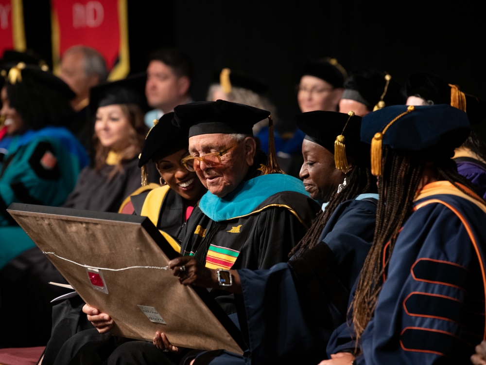 Tisha Edwards, left, and Wendy Shaia admire the framed UMB Doctor of Public Service honorary degree held by Ronald Chisom.